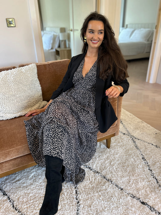 Black blazer with ruched sleeves worn open over a patterned dress.