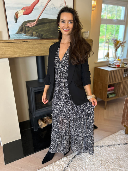 Black blazer with ruched sleeves worn open over a black-and-white patterned dress.