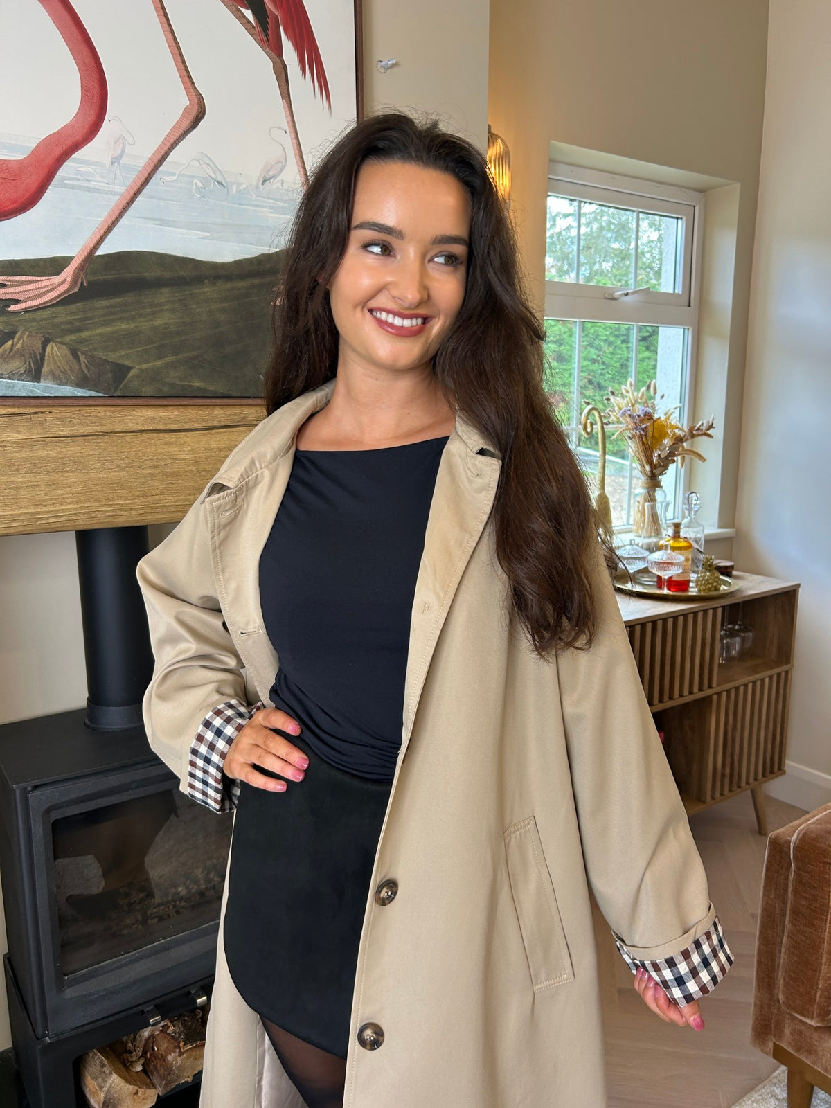 Taupe trench coat worn open, with a button front, notched lapels and check-pattern turn-back cuffs.